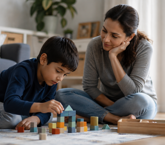 A child builds with colorful blocks while a woman observes, illustrating engaging activities for understanding autism spectrum disorder.